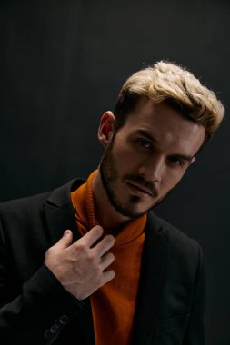 Ceketli yakışıklı bir adamın portresi ve elleri koyu arkaplan fotokopisi ile turuncu bir kazak.