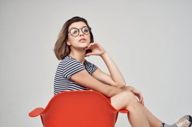 Kırmızı sandalyede oturan neşeli kadın şık moda pozu veriyor.