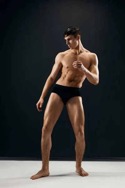 Uomo sportivo in mutandine nere con nudo corpo muscolare sfondo scuro — Foto Stock