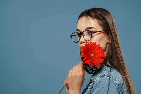 Vacker brunett bär glasögon röd blomma nära ansiktet Glamor blå bakgrund — Stockfoto