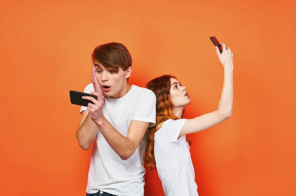 Ein Mann und eine Frau in weißen T-Shirts, die Telefone in der Hand halten — Stockfoto