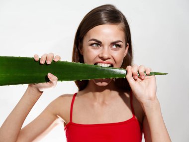 Dişlerinde aloe yaprağı ve kırmızı tişörtlü çıplak omuz modeli olan duygusal bir kadın.