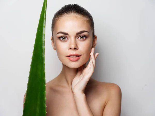 Mulher bonita corre a mão sobre o rosto e folha de aloés verde em um fundo leve — Fotografia de Stock