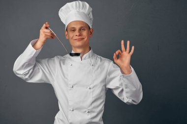 Elinde kepçeyle beyaz bornozlu bir şef yemek lokantası pişiriyor.