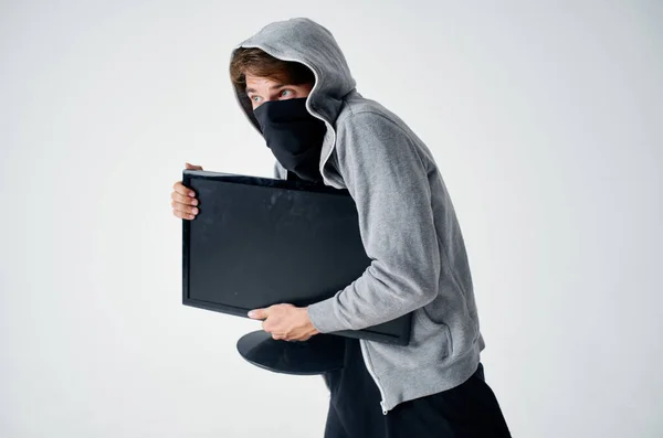 Чоловік з капюшоном у масці краде технічний комп'ютер — стокове фото