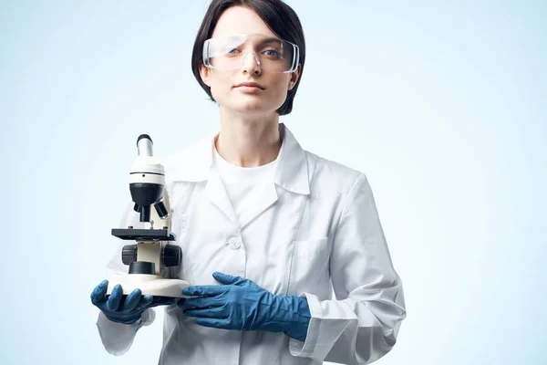 एक पेशेवर चिकित्सा प्रौद्योगिकी के हाथों में एक माइक्रोस्कोप के साथ एक सफेद कोट में महिला प्रयोगशाला सहायक — स्टॉक फ़ोटो, इमेज