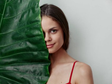 Güzel kadın yüzünün yarısını yeşil yapraklı büyüleyici bir bakışla kaplıyor.