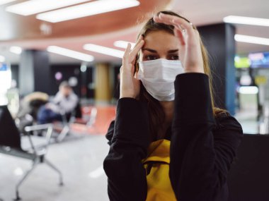 Tıbbi maske takan bir kadın havaalanı yorgunluğunu bekliyor.