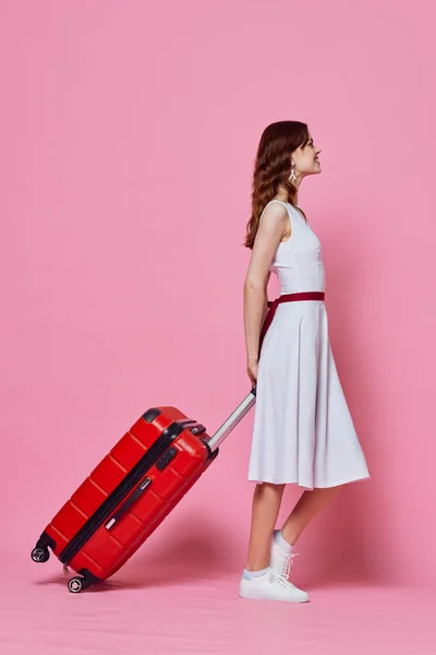 Женщина с красным чемоданом белое платье эмоции путешествия розовый фон — стоковое фото