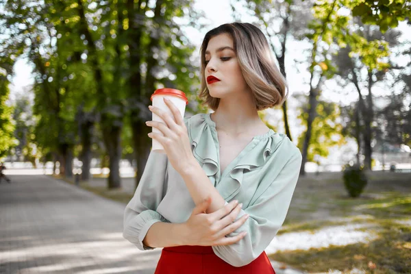 Rubia alegre con una taza de café al aire libre caminando en el parque — Foto de Stock