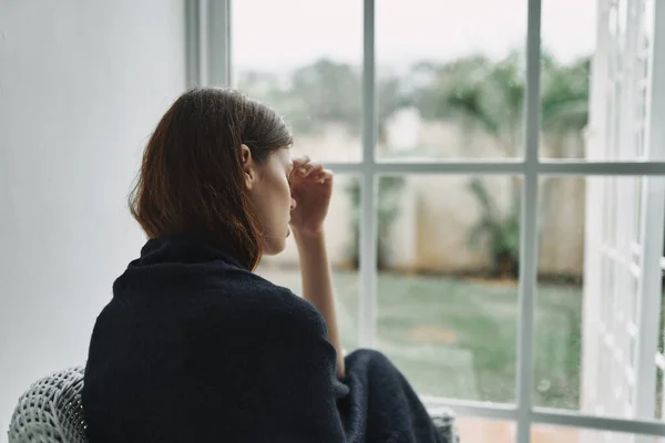 Ženy doma se přikryla přikrývkou a dívá se z okna interiéru odpočinku — Stock fotografie
