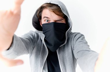 Kapüşonlu bir adam yüzünü maskeli bir zorbanın içinde gizler.