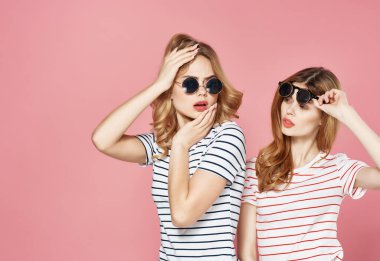 İki kız arkadaş çizgili tişörtler içinde yan yana durur. Gözlükler moda yaz pembe arka plan.
