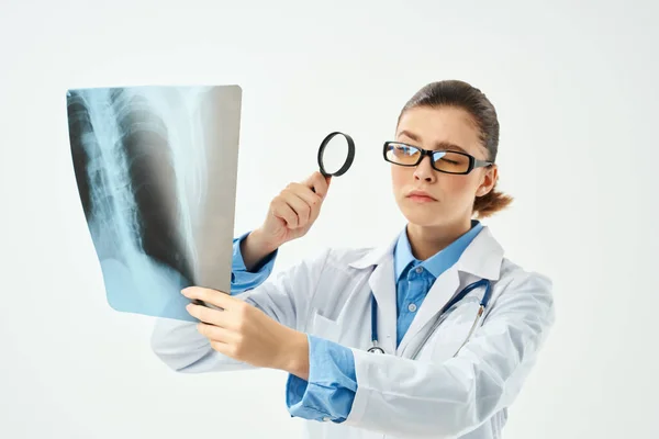 Медсестра в білому пальто дивиться через збільшувальний стакан на рентгенівському — стокове фото