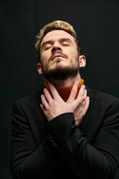 Aantrekkelijke blonde man op een donkere achtergrond in een oranje trui en jas — Stockfoto