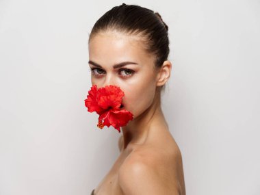 Ağzında kırmızı çiçek olan güzel bir kadın çıplak omuzlarını yakın plan açık arka plan.