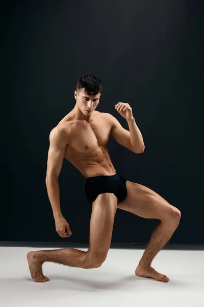Man med pumpas upp muskulös kropp svarta trosor poserar mörk studio bakgrund — Stockfoto