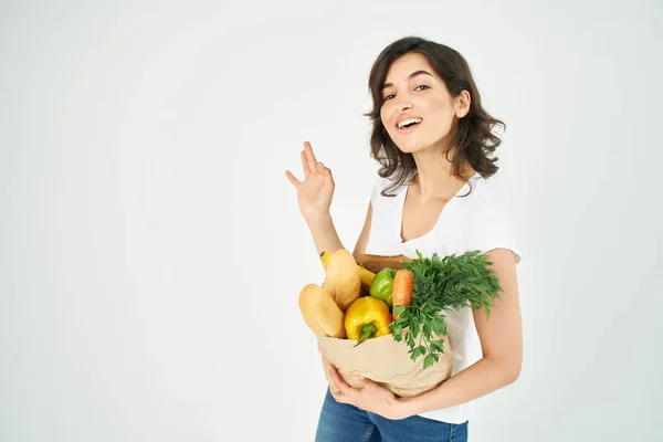 Linda morena en una camiseta blanca una bolsa de comestibles gesticulando con un supermercado de mano —  Fotos de Stock