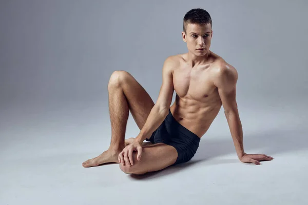 Спортивный человек мускулистое тело позируя сидя на полу тренировки — стоковое фото
