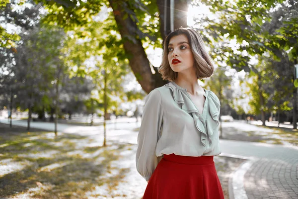 Žena v červené sukni procházky v parku stromy životní styl — Stock fotografie