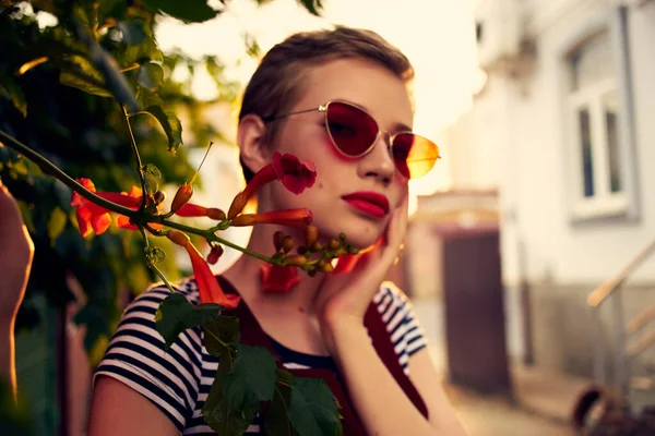 Kort hår kvinna bär solglasögon utomhus blommor dekoration — Stockfoto