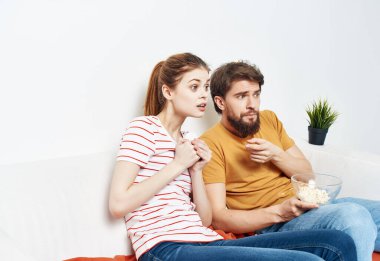Komik adam ve kadın kanepede eglenceli bir şekilde patlamış mısır yiyor.