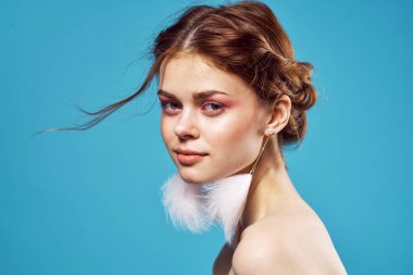 Çıplak omuzlu ve tüylü küpeli moda zevkli kozmetik ürünleri olan bir kadın.