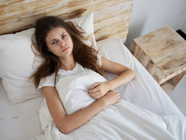 Недовольная женщина лежит в постели под одеялом под утренним видом сверху — стоковое фото