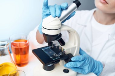 Tıbbi giysi mikroskop kimyasal çözümler araştırmasında kadın laboratuvar asistanı.