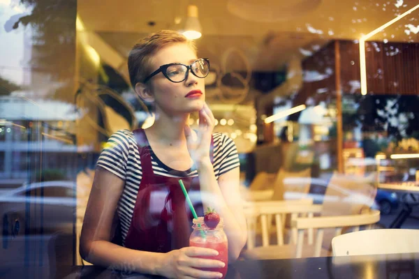 3.女人从窗户朝外看街上的咖啡店,喝着鸡尾酒,享受着生活 — 图库照片