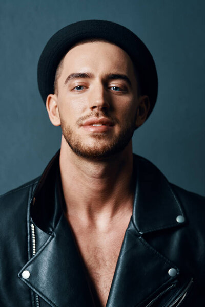 Cheerful fashionable man in leather jacket posing against dark background