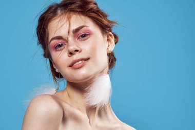 Çıplak omuzlu, parlak makyajlı, mavi arka planlı bir kadın.