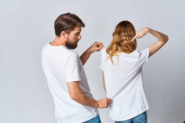 Man och kvinna i vita t-shirts stå med ryggen ljus bakgrund mockup — Stockfoto