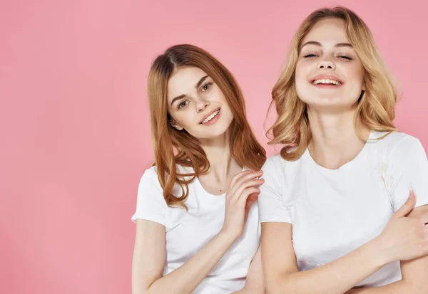 Två systrar vit t-shirts kram vänskap känslor rosa bakgrund — Stockfoto