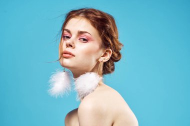 Parlak makyajlı, tüylü küpeli, yakın plan poz veren bir kadın.