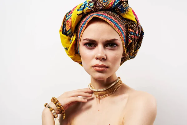 Όμορφη γυναίκα κρατώντας το κεφάλι της διακόσμηση πολύχρωμο τουρμπάνι φως μόδας φόντο — Φωτογραφία Αρχείου