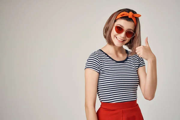 Duygusal kadın güneş gözlüğü takıyor, çizgili tişört giyiyor modern tarz açık arkaplan pozu veriyor. — Stok fotoğraf