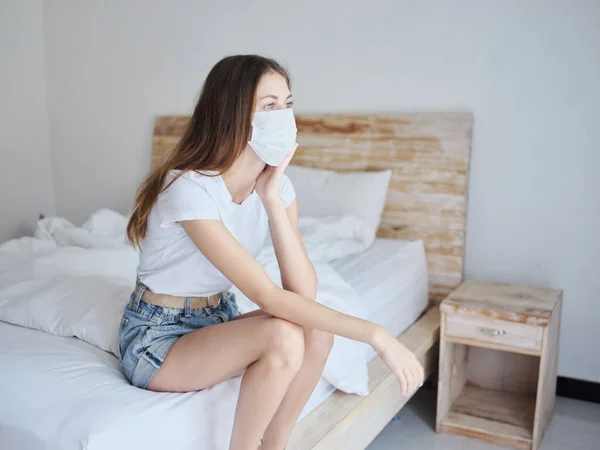 Donna in maschera medica seduta sul letto in camera isolata pandemia di quarantena — Foto Stock