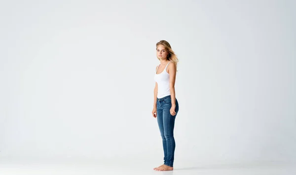 Bella bionda in jeans si trova a piedi nudi sul pavimento isolato modello di sfondo — Foto Stock