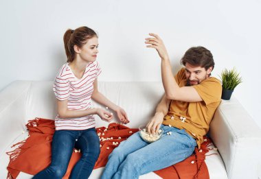 Genç bir aile patlamış mısırla kanepede oturmuş film seyrediyor.