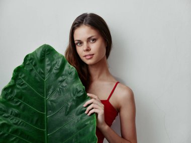 Kırmızı mayo giymiş kızıl saçlı kadın arka planında palmiye yaprağı tutuyor.