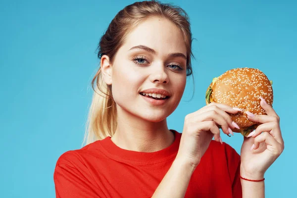 Vrolijk vrouw in rood t-shirt hamburger in handen fast food blauw achtergrond — Stockfoto