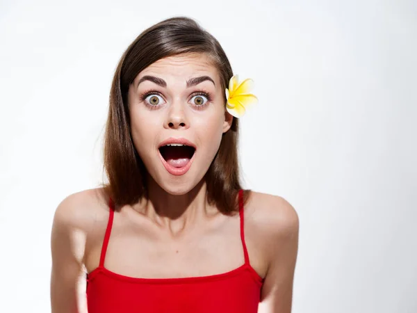Surprised woman with wide open mouth on a light background and a yellow flower in her hair — стоковое фото