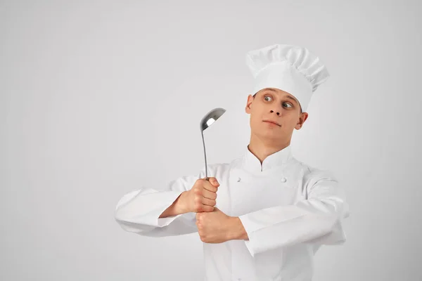 Un uomo in uniforme chef con un mestolo in mano preparare cibo sfondo luce — Foto Stock