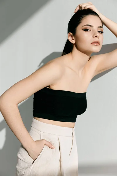 Beautiful brunette with fashionable makeup and white pants leaning against the wall in the room — Fotografia de Stock