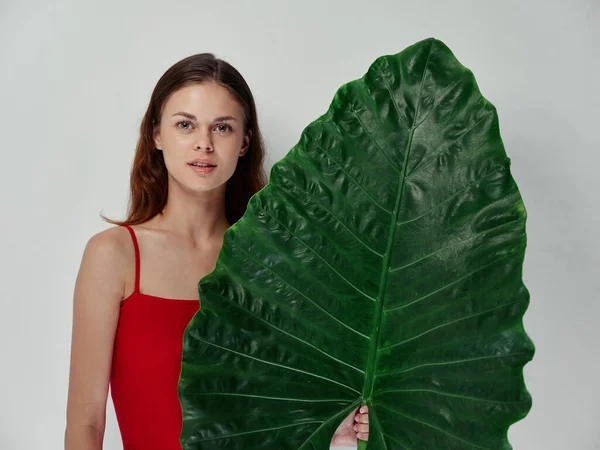 A woman in a red t-shirt holds a green leaf in her hand clean skin and a natural look —  Fotos de Stock