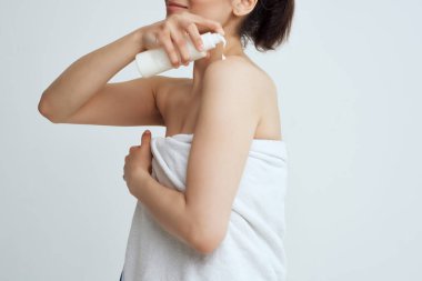 Havlu giymiş bir kadın çıplak omuzlarına losyon sürüyor.