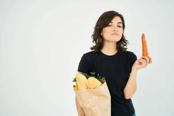 Женщина в черной футболке в упаковке с продуктами здоровой доставки продуктов питания легкий фон — стоковое фото