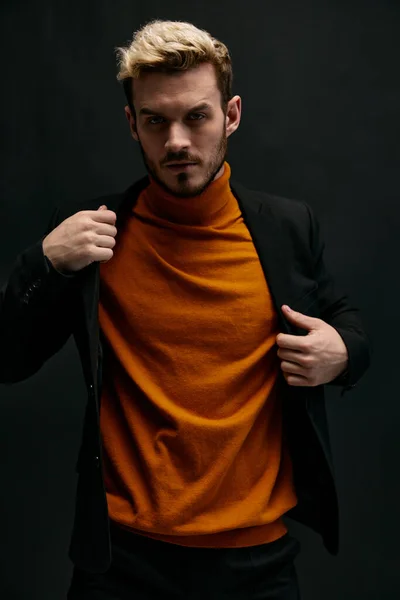 Un hombre en un suéter naranja y una chaqueta sobre un fondo oscuro retrato rubio de cerca —  Fotos de Stock