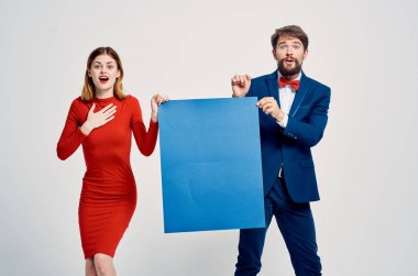 Kırmızı elbiseli bir kadının yanında takım elbiseli bir adam. Mavi poster reklamı.